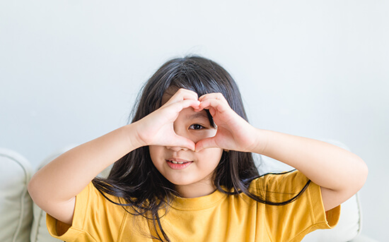 Child making a heart around their eye